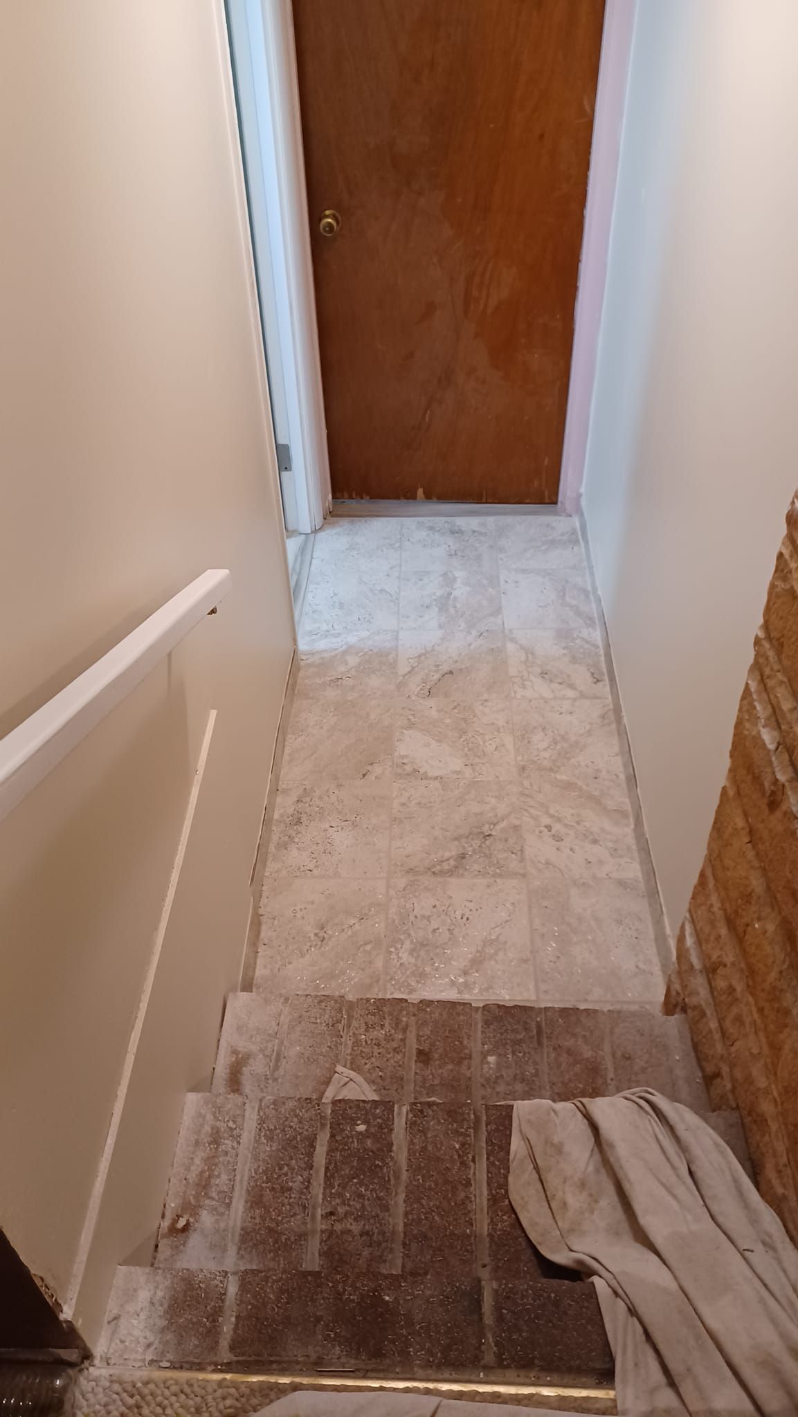 Narrow hallway with a closed wooden door and a small carpeted landing, viewed from a stairwell.