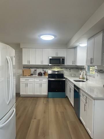 Bright modern white kitchen with stainless appliances, wood floor, and large island countertop