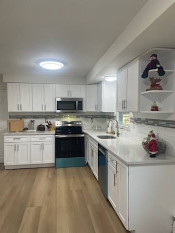 Bright white kitchen with stainless appliances, wood floor, and holiday decorations on shelves.