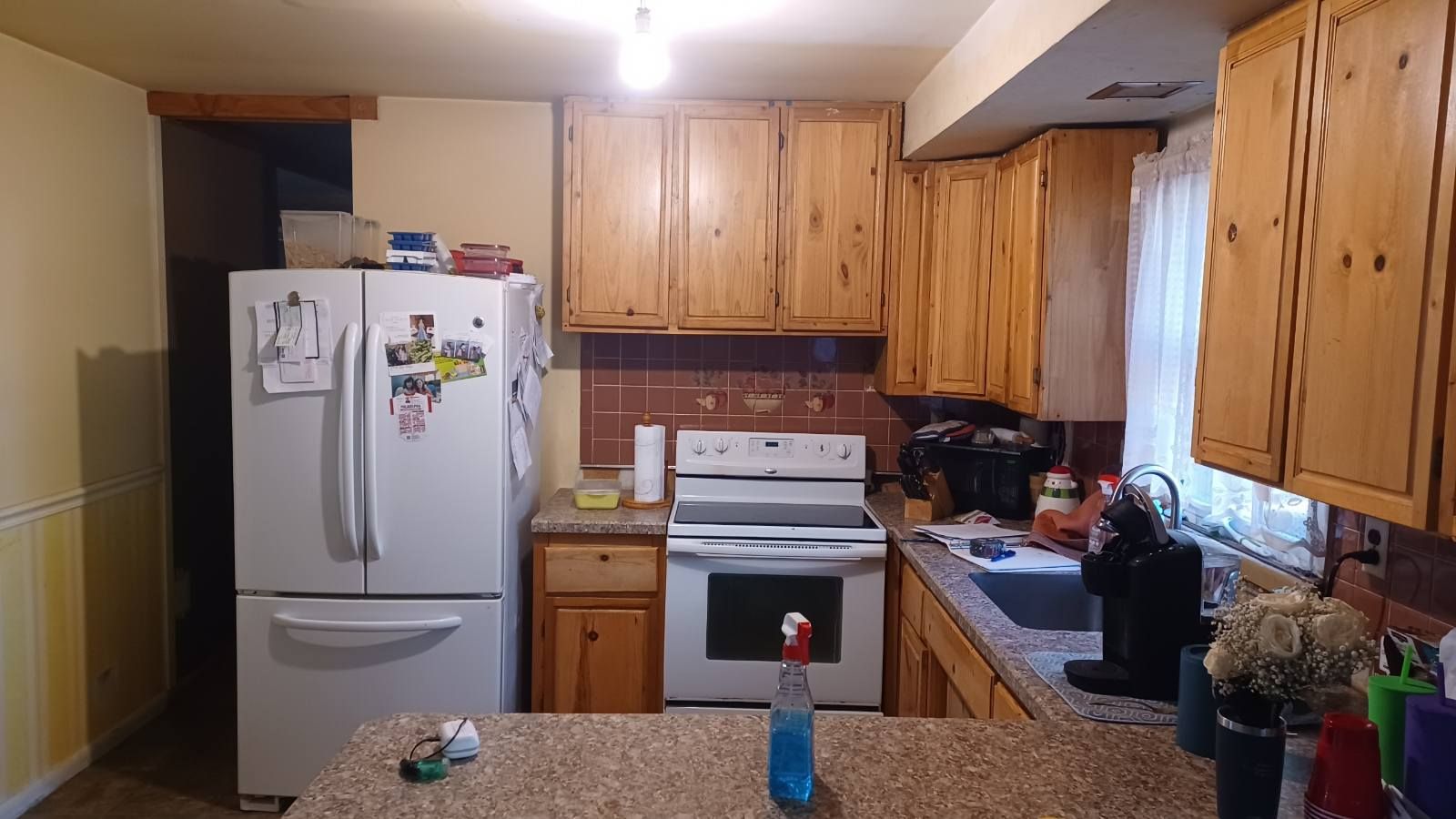 Small kitchen with wooden cabinets, white refrigerator and stove, and a speckled countertop in the foreground