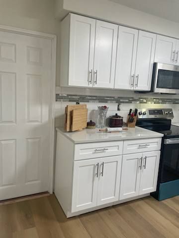 White kitchen with cabinets, countertop, stove, and a door on the left