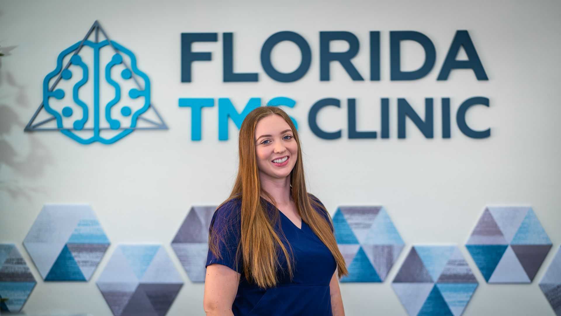 Woman in blue scrubs smiles in front of the 