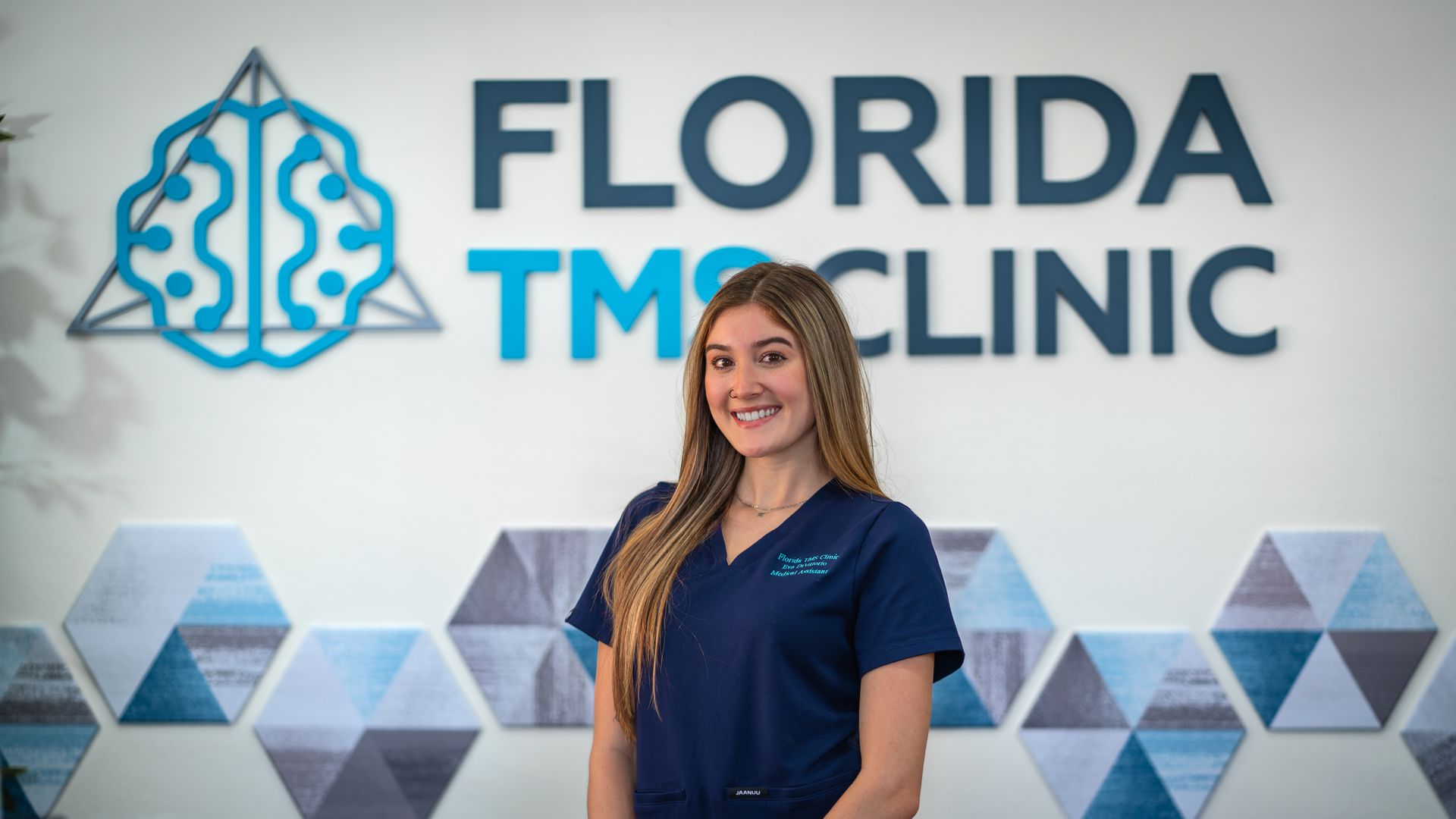 A woman in blue scrubs smiles in front of a 