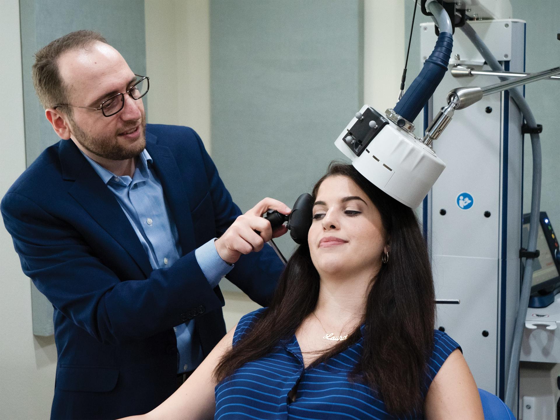 Technician adjusts a head-mounted device on a seated woman in a lab setting