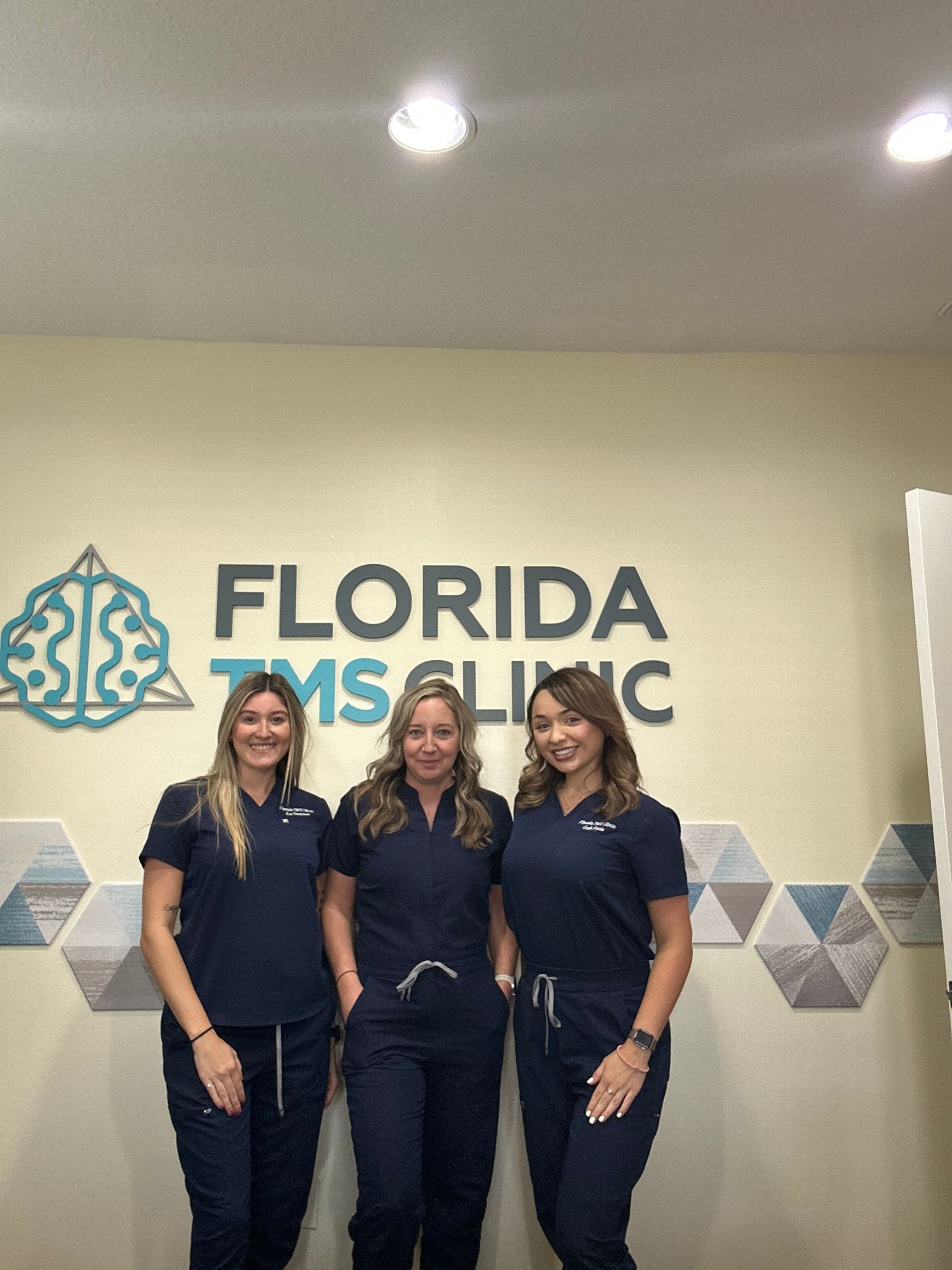 Three women in blue scrubs pose in front of a clinic sign that reads 