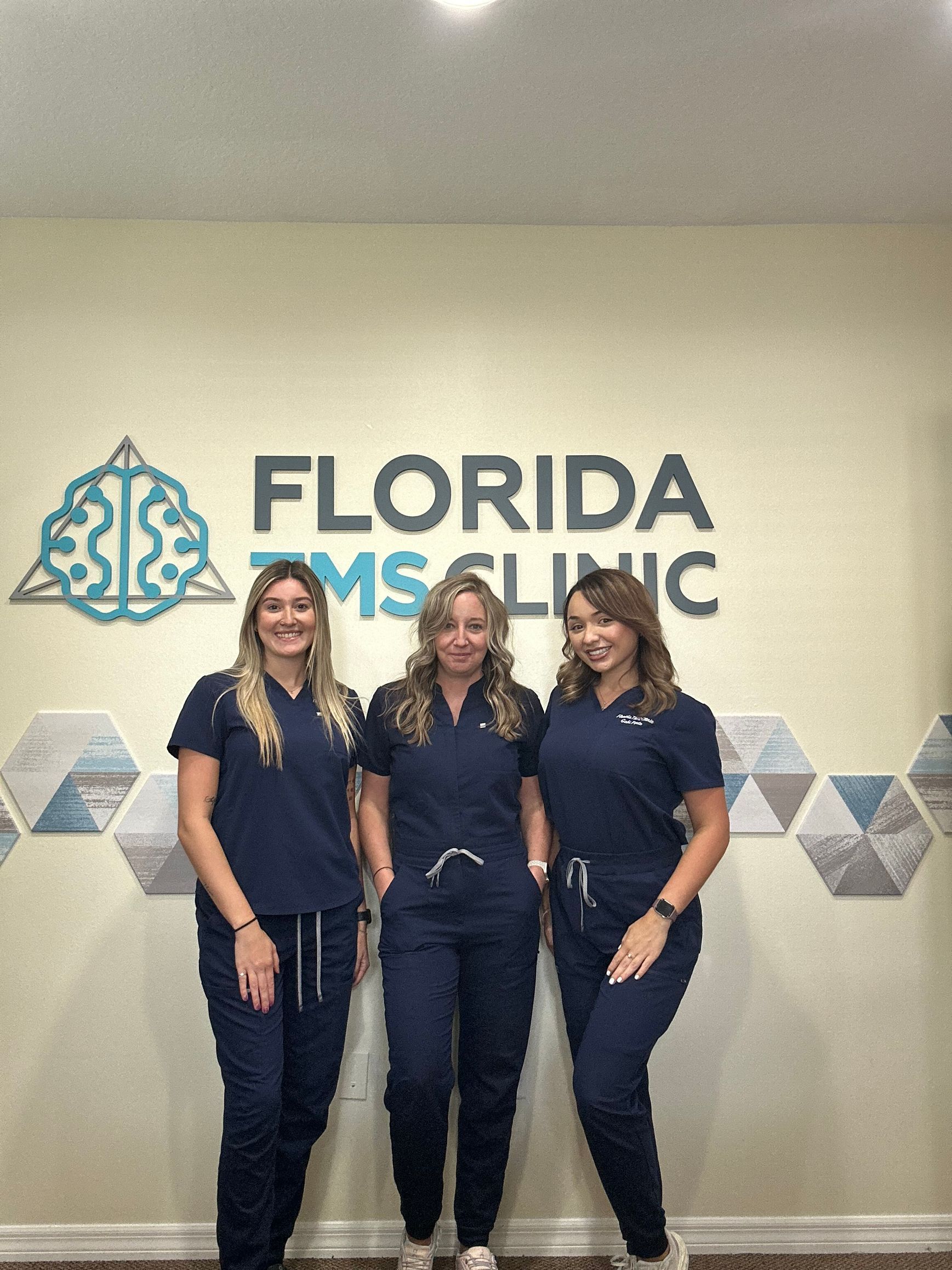 Three women in blue scrubs pose in front of 