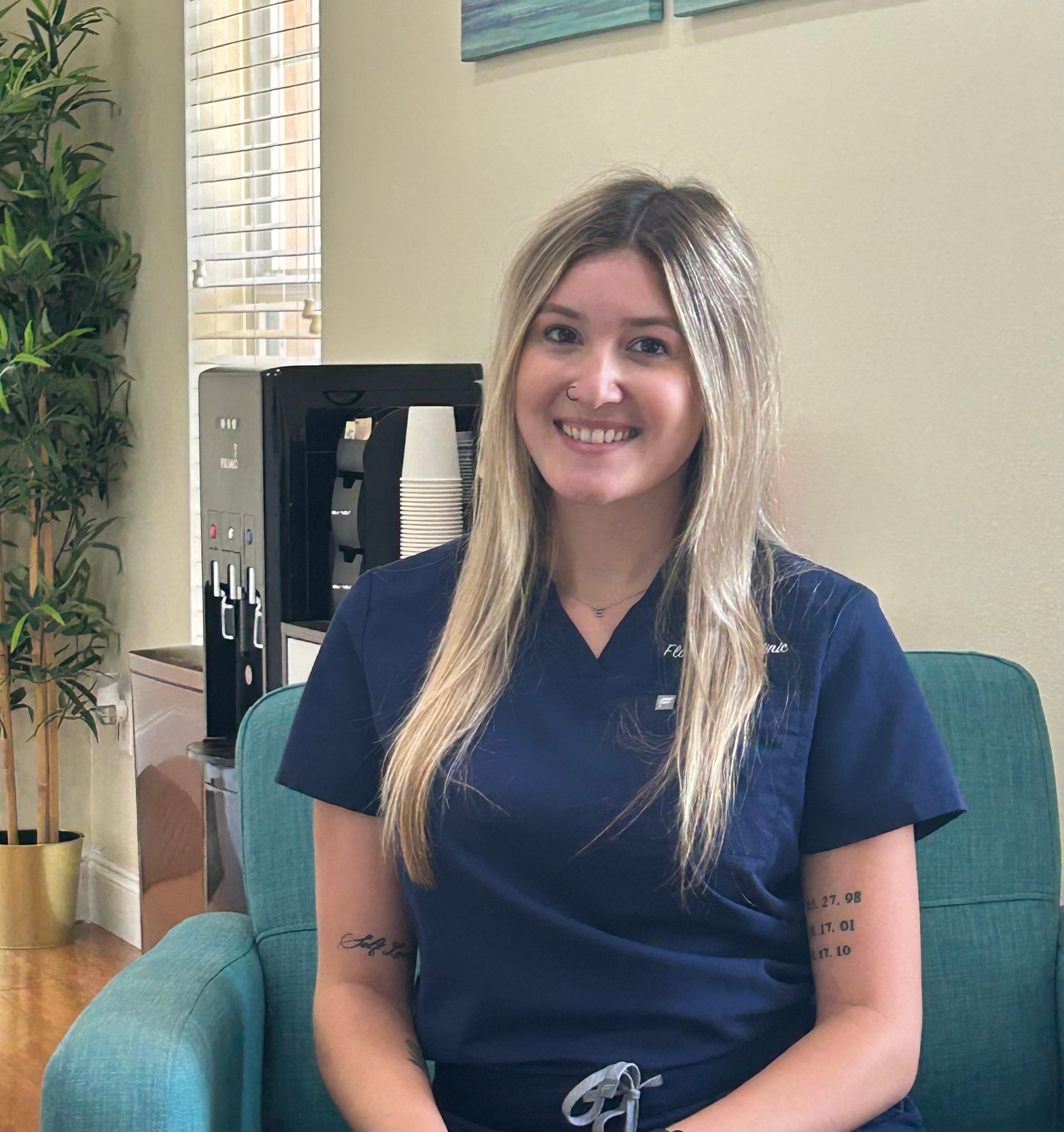 Woman with blonde hair smiling in blue scrubs, seated in a teal chair.