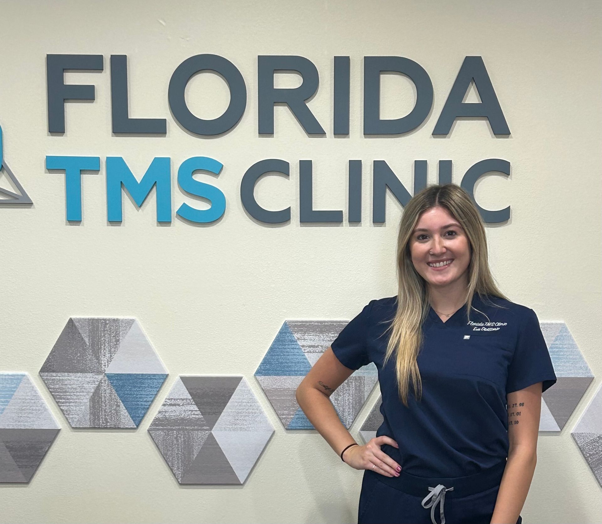 Woman in scrubs stands in front of a 