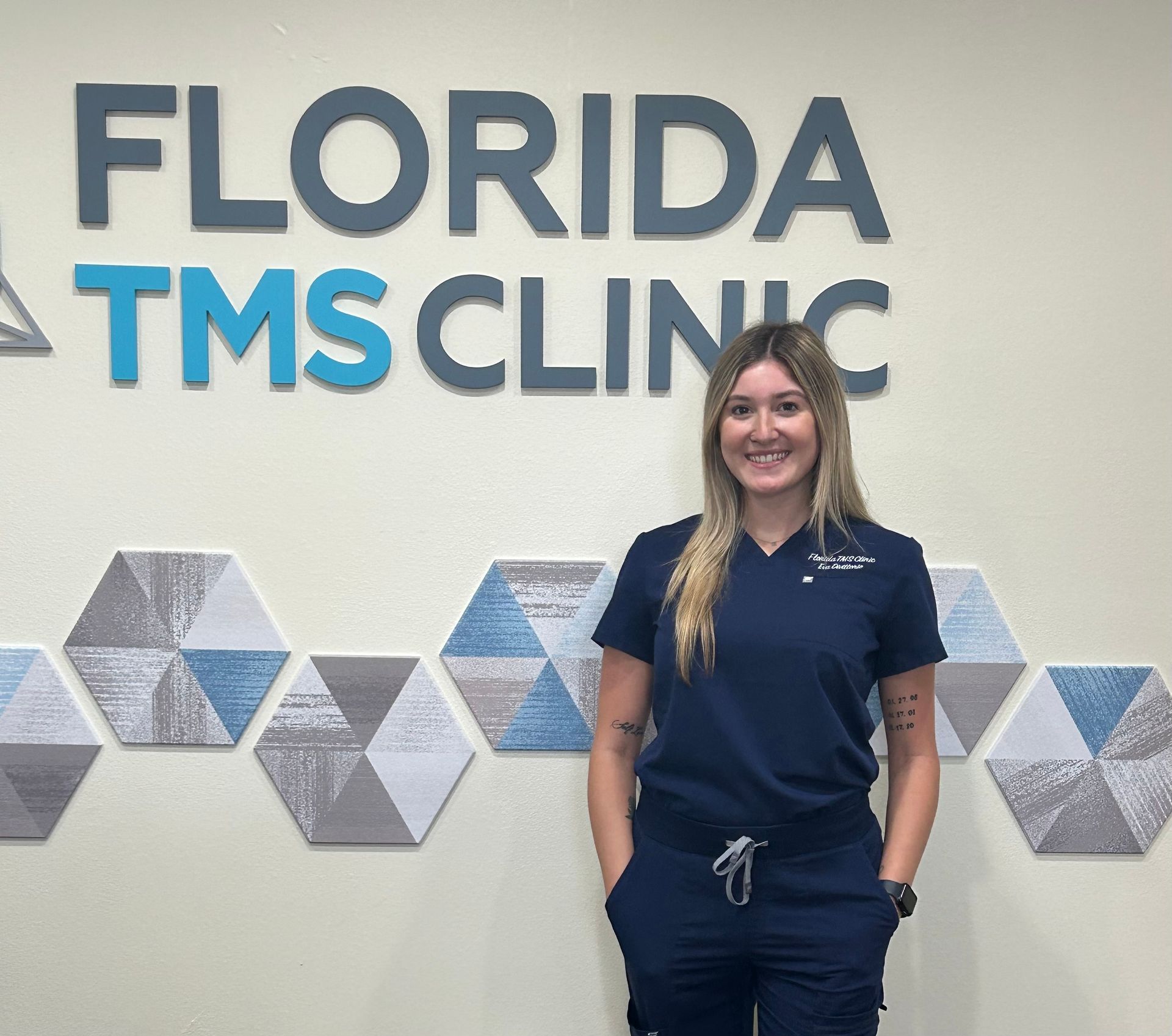 Woman in blue scrubs smiles in front of the 