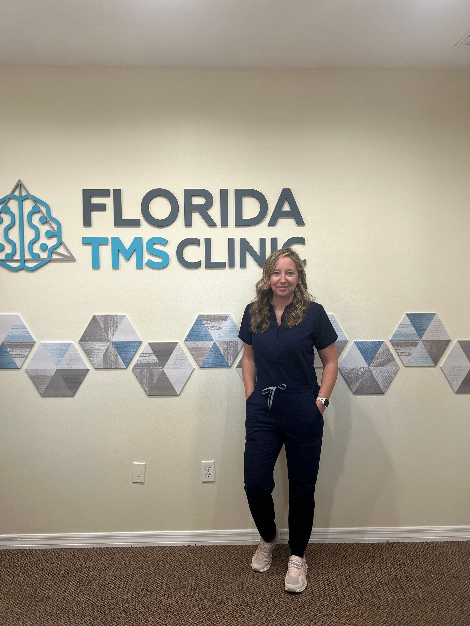 Woman in scrubs stands in front of the Florida TMS Clinic sign.