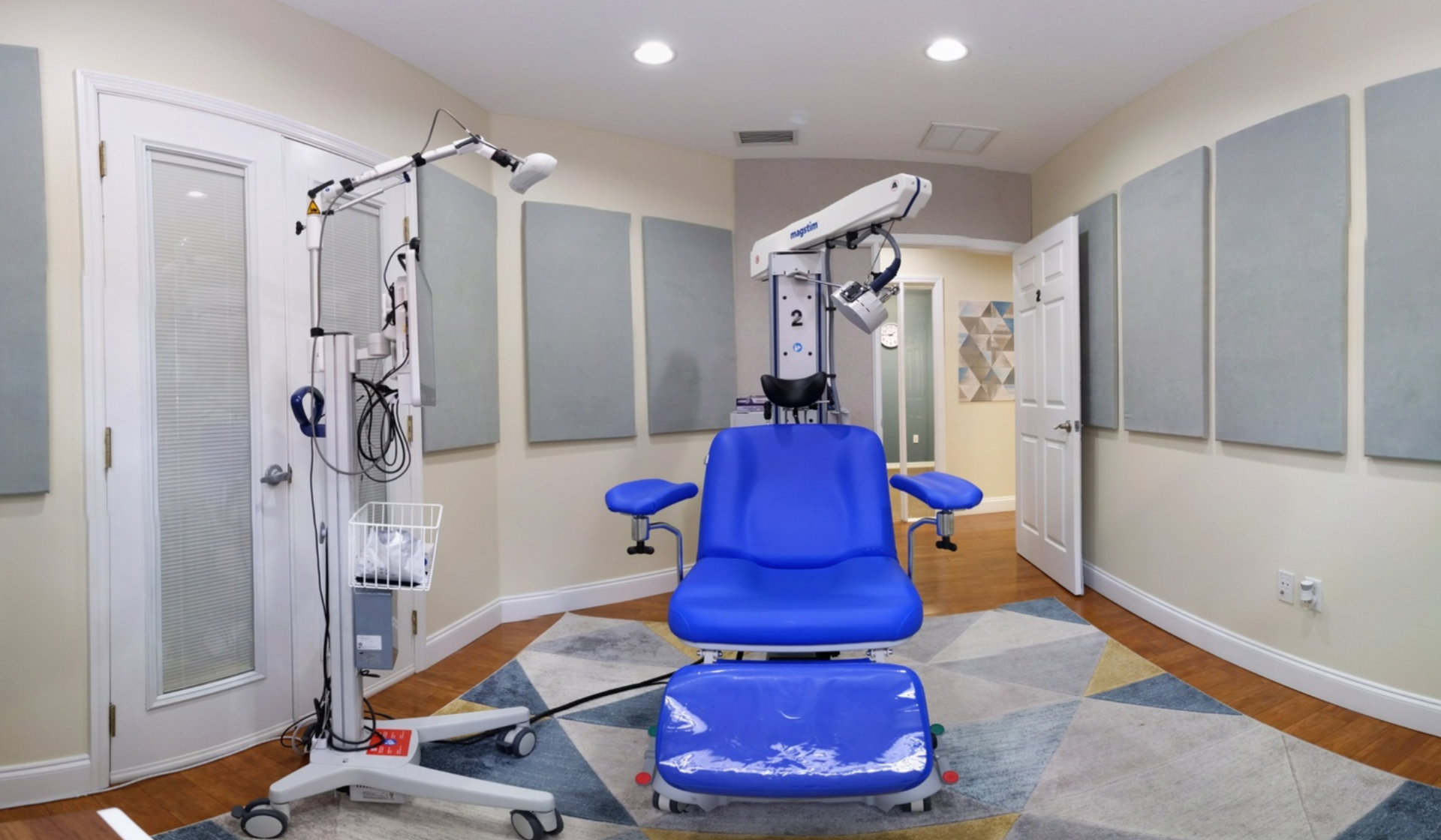 A medical examination room featuring a blue chair with attached equipment, a diagnostic device, and soundproofing panels.