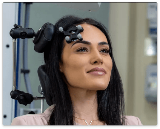 Woman with dark hair, wearing a medical head device. She is looking upwards and smiling in a clinic setting.