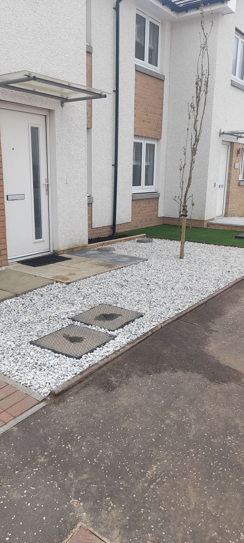 Front of a house with a gravel driveway and two utility covers beside a paved path.