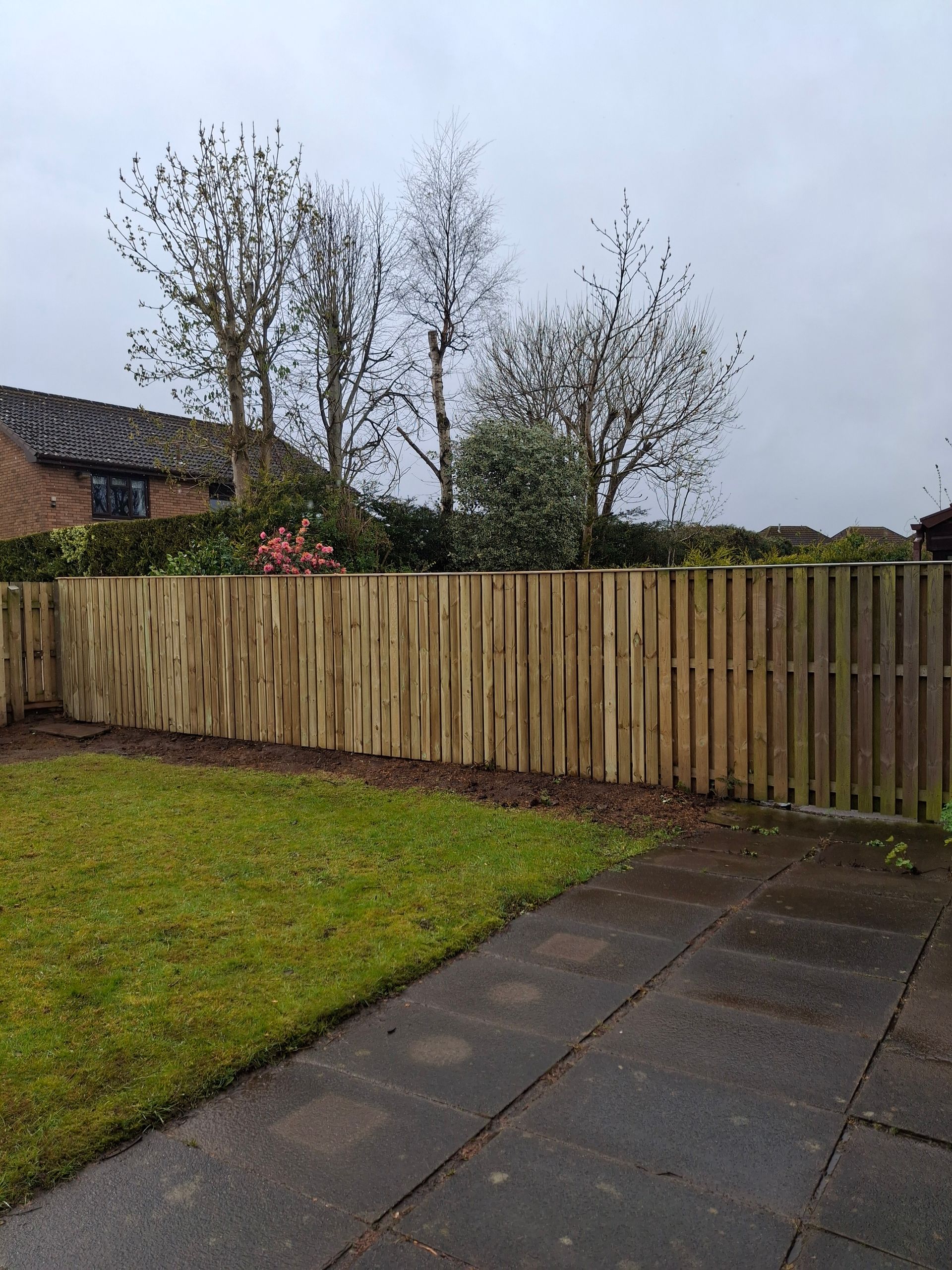 Backyard with a wooden fence, grass lawn, paved patio, and cloudy sky