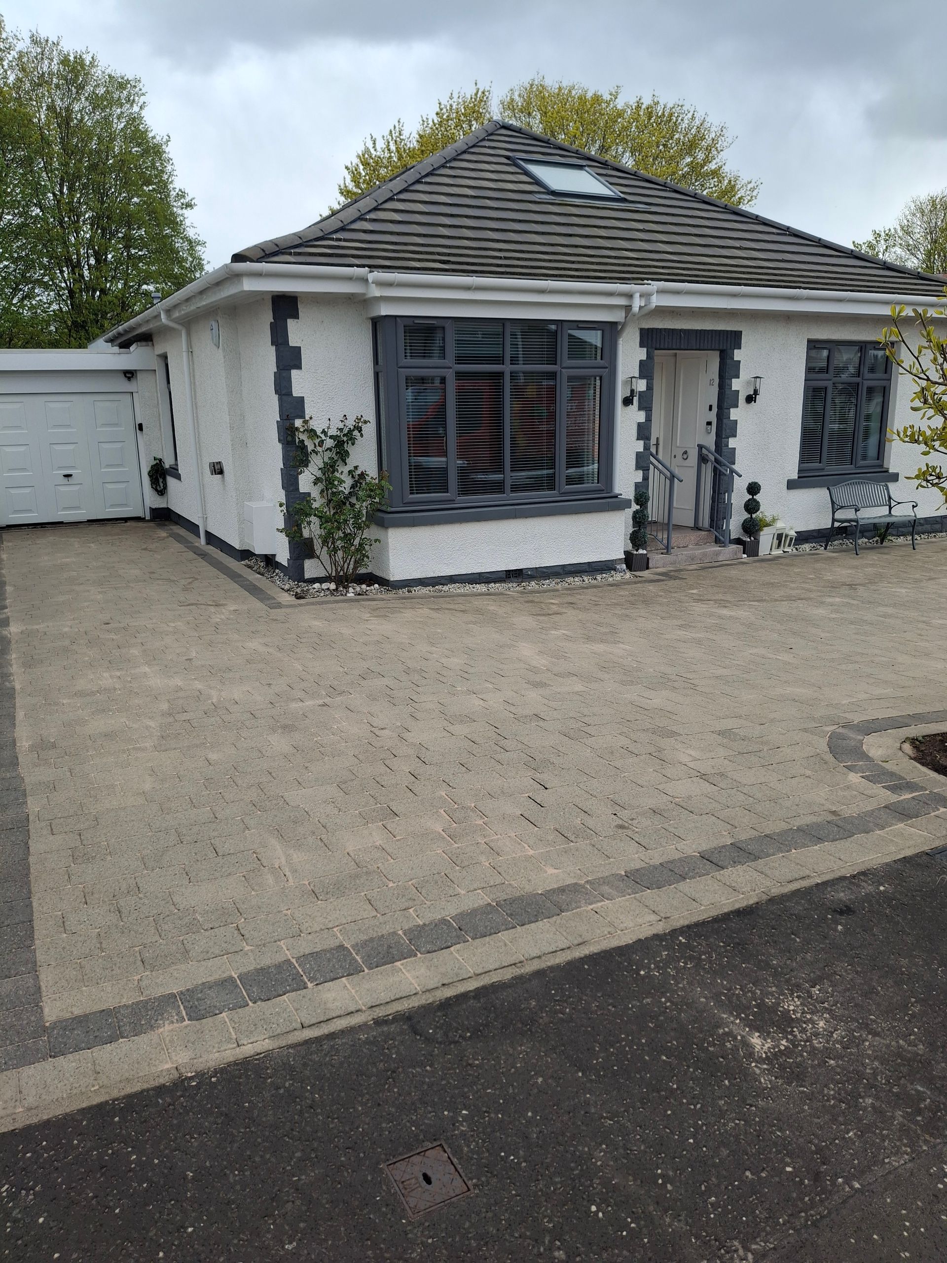 Small white house with gray roof, gravel driveway, and attached garage under a cloudy sky