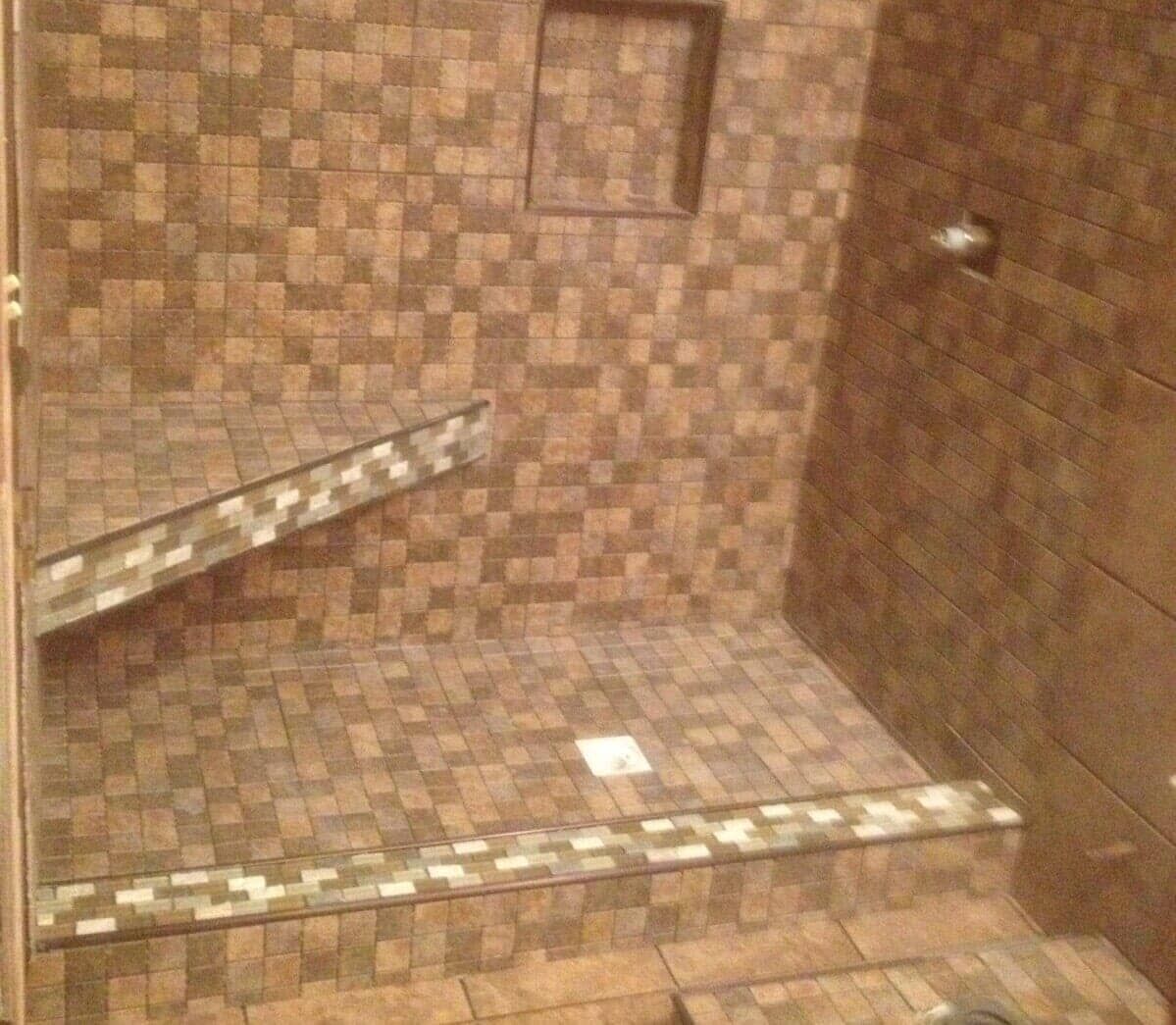 A brown tiled walk-in shower with a built-in bench, a wall niche for toiletries, and a decorative mosaic border.