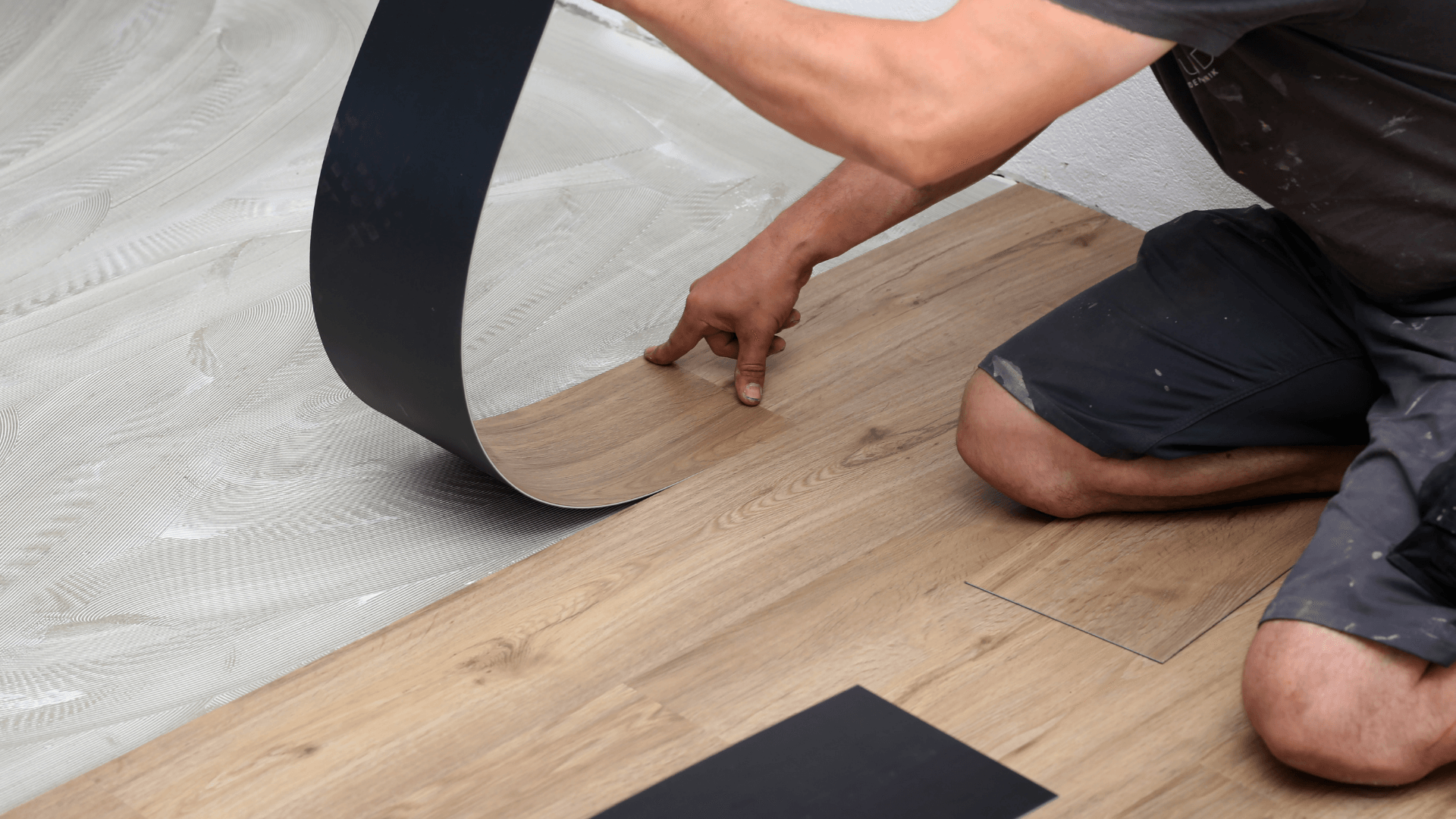 A person kneeling on a floor installs wood-look vinyl planks over a layer of wet adhesive.
