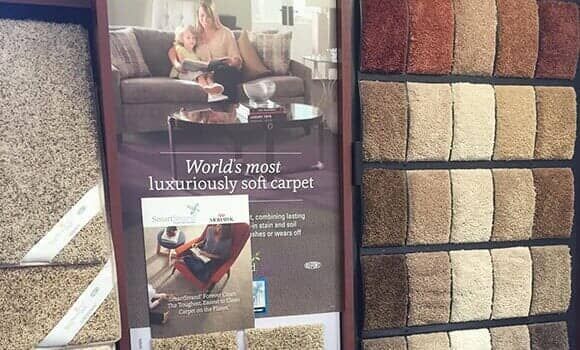 A display of carpet samples in various neutral tones, alongside a promotional poster for