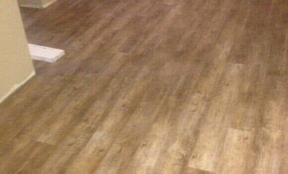 Brown wood-look plank flooring installed in a room, with a glimpse of a wall corner and a white trim piece.