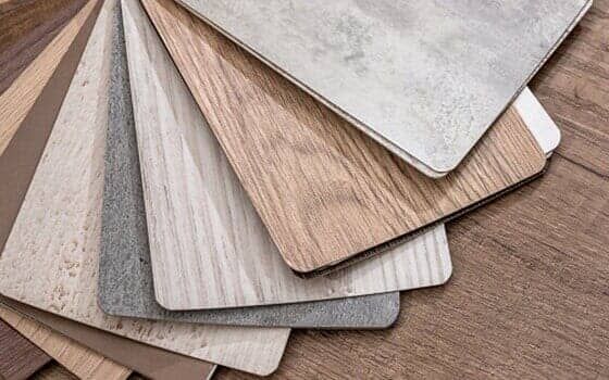 A fan-shaped sample set of wood-grain and stone-textured flooring tiles in various shades of brown, gray, and cream.