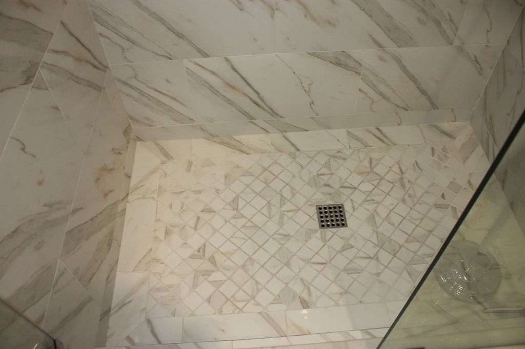 A walk in shower with marble tiles and a drain.