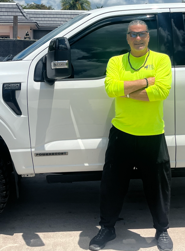 A man is standing next to a blue truck in a garage.