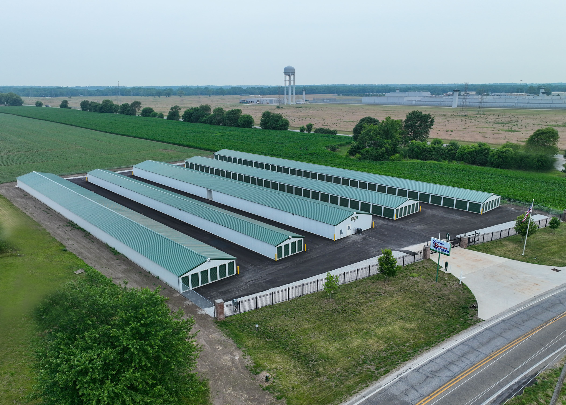 Storage units with green roofs, next to a field, and a road in a rural area.
