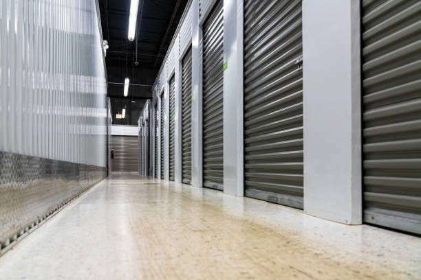 Hallway of storage units with closed, gray roll-up doors and a glossy floor.