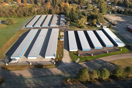 Storage Solutions facility top view — Storage in Terre Haute, IN Aerial view of storage units, rows of white buildings with blue doors, surrounded by trees and fields.