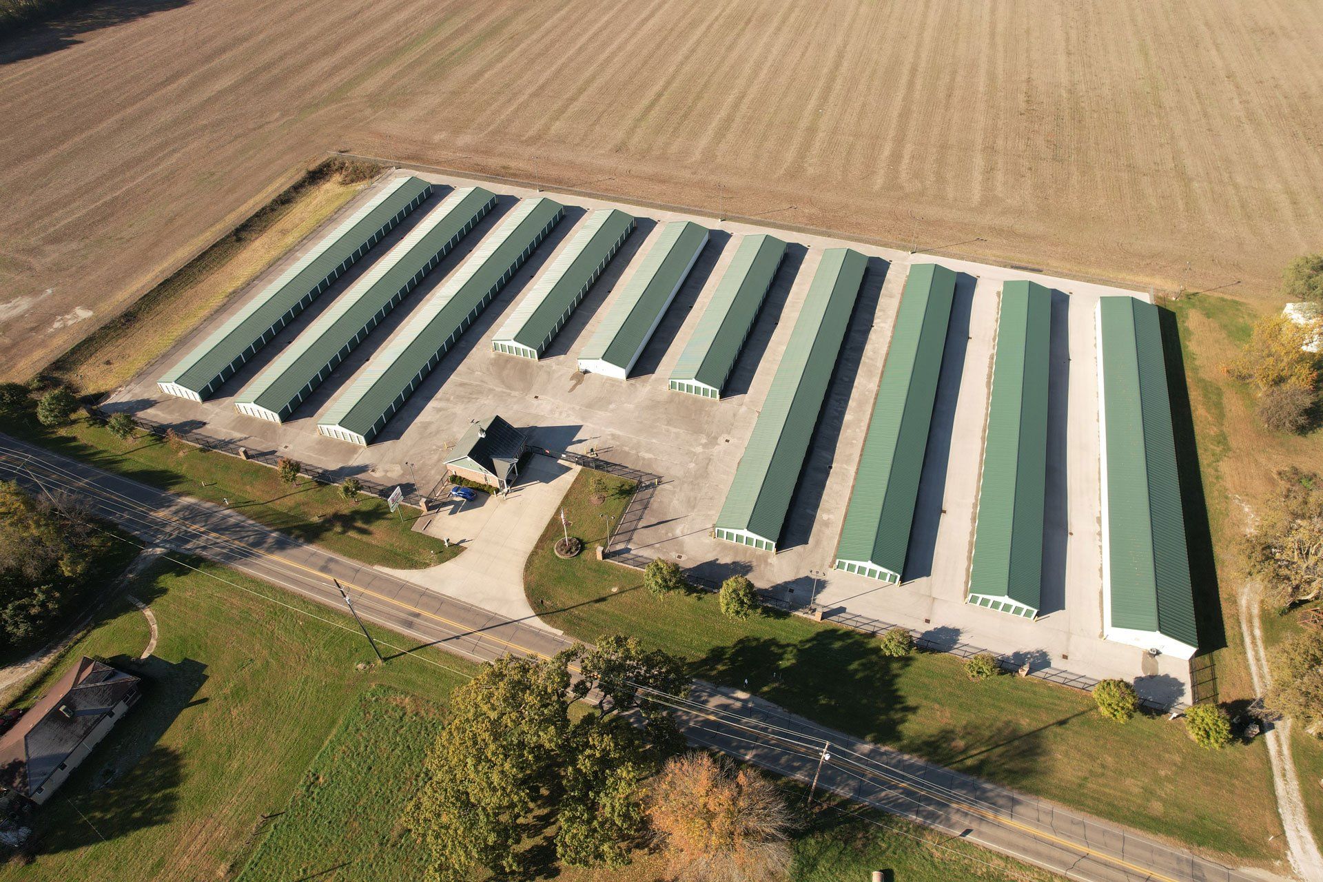 Aerial view of a storage facility with rows of green-roofed buildings on a concrete pad surrounded by farmland.