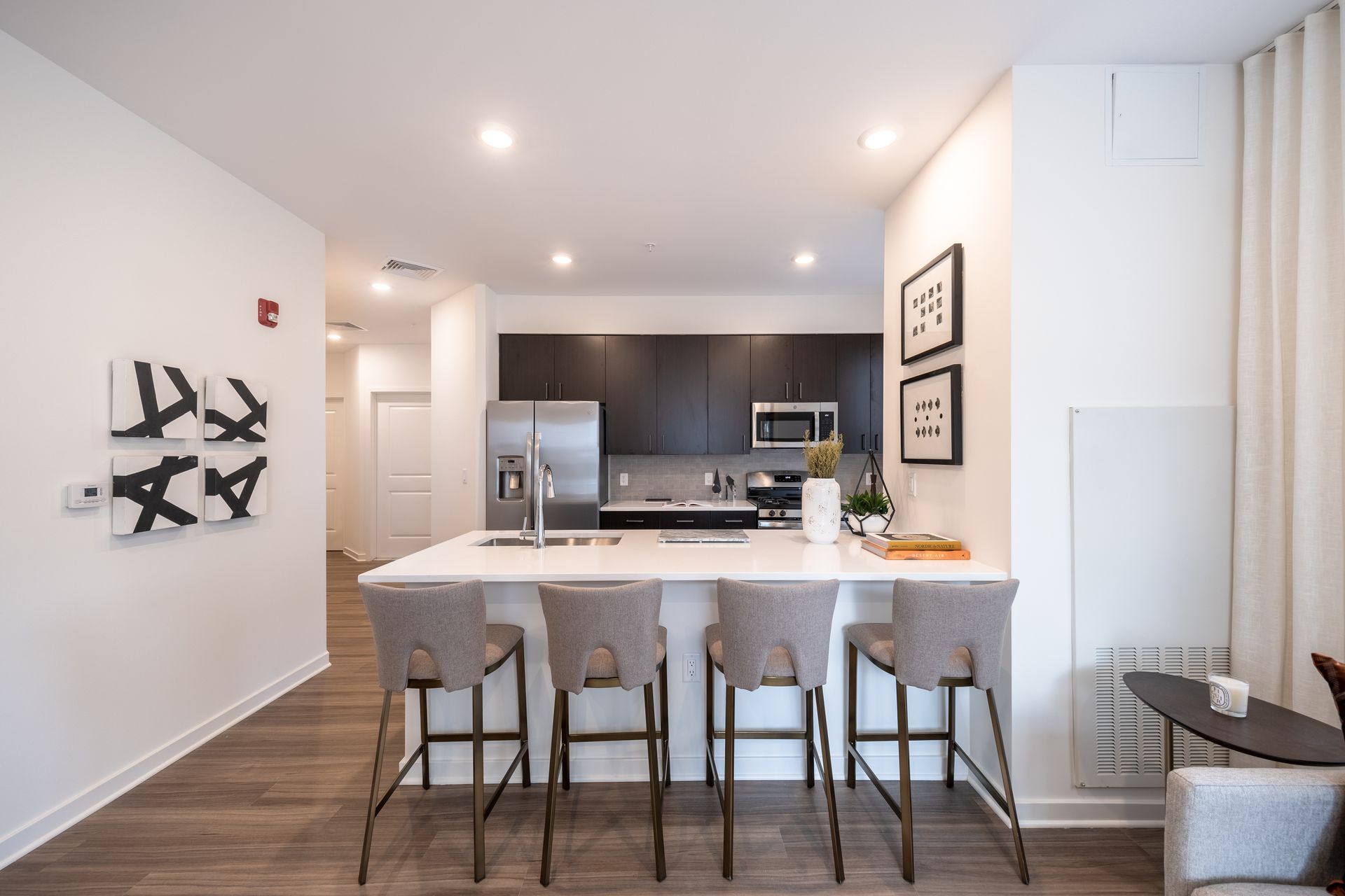 Modern kitchen with island, seating, stainless steel appliances, and art on white walls.
