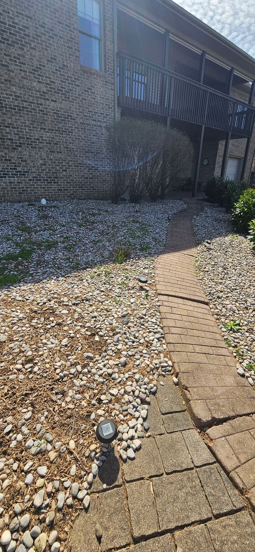 Gravel yard beside a brick house with a concrete path and small garden light in the foreground