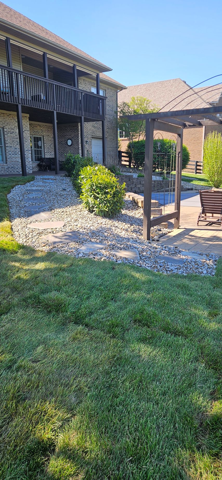 Brick apartment building with covered patio, stone landscaping, and green lawn under a bright blue sky