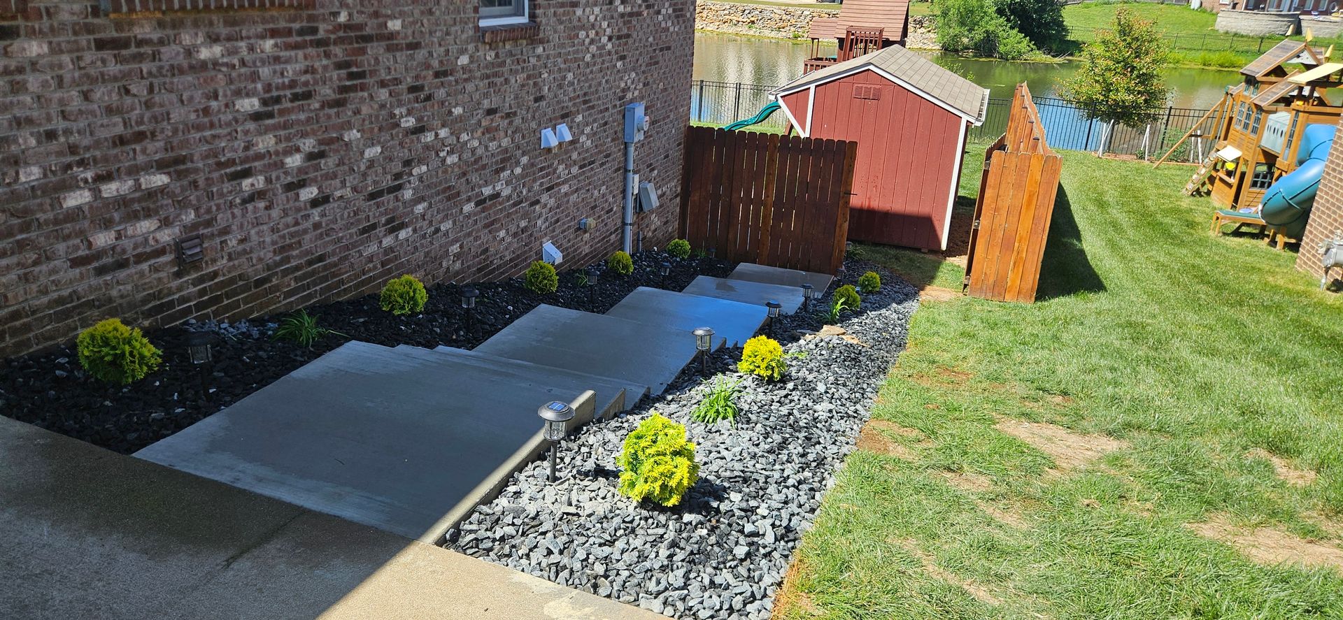 Small garden bed beside a brick wall, with black gravel, paving slabs, and a yellow flower centerpiece.