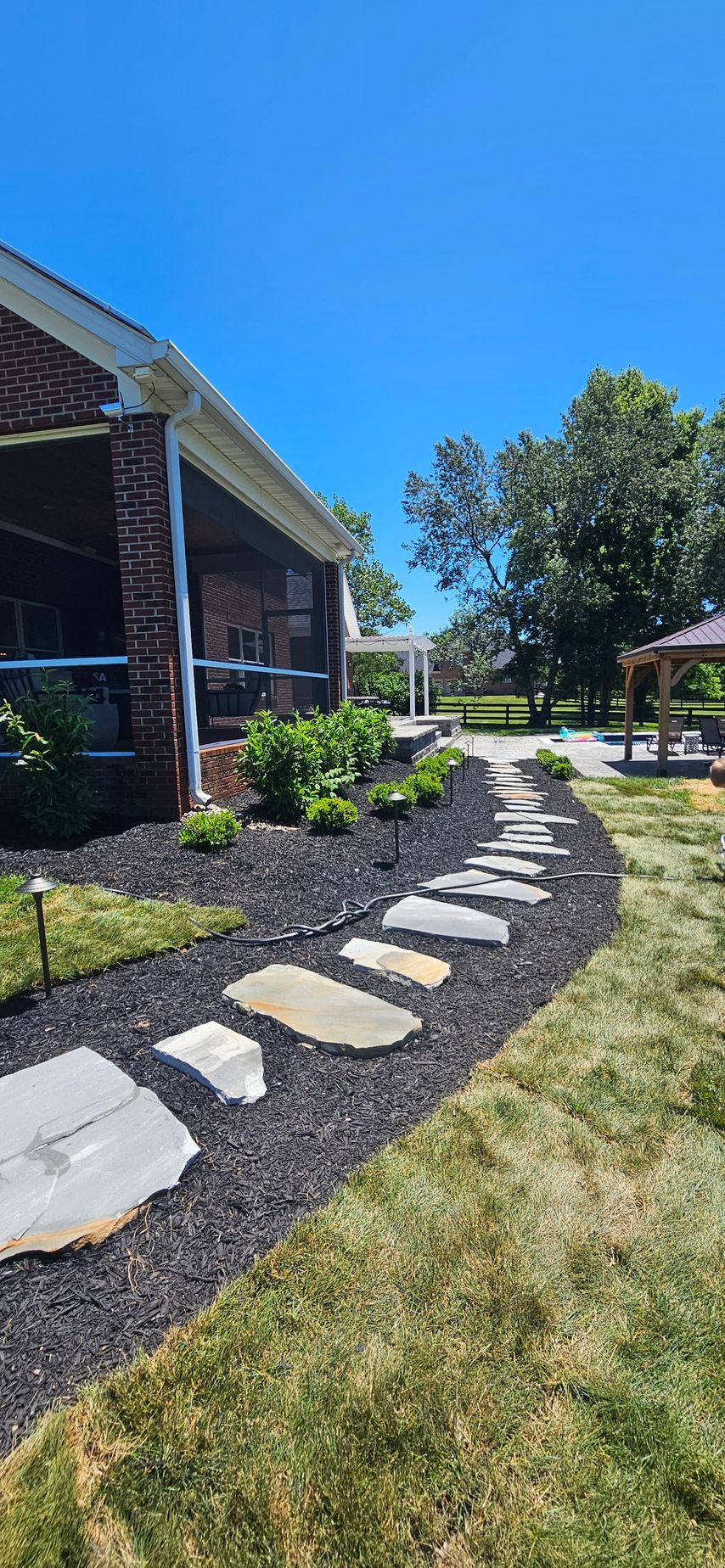Stone stepping path beside a brick house and landscaped garden under a bright blue sky