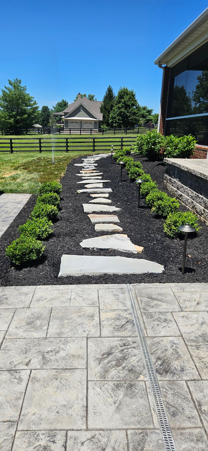 Stone path with stepping stones through a landscaped yard toward a gazebo under a blue sky