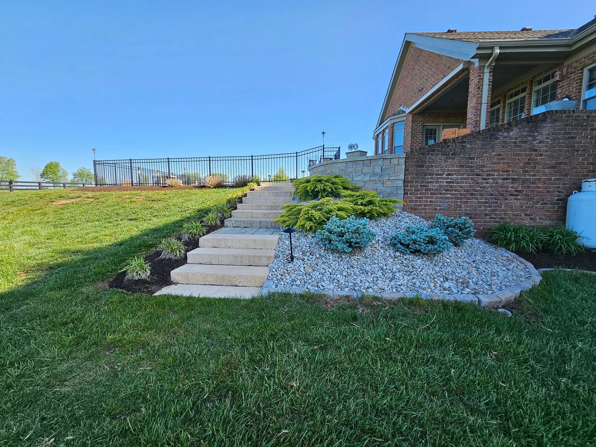 Stone steps lead up a grassy hill, with landscaping and a brick building to the right.