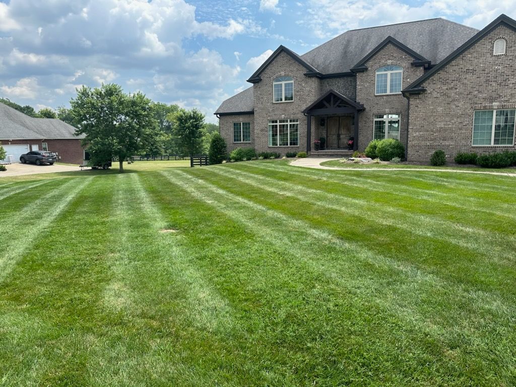 Large brick suburban house with a wide striped green lawn under a cloudy sky
