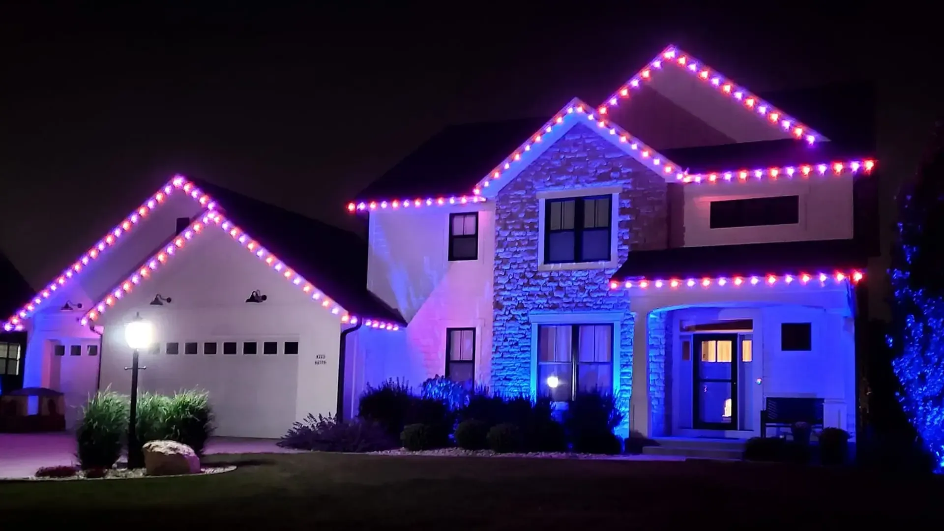 House at night, decorated with Christmas lights, with a car in the driveway.