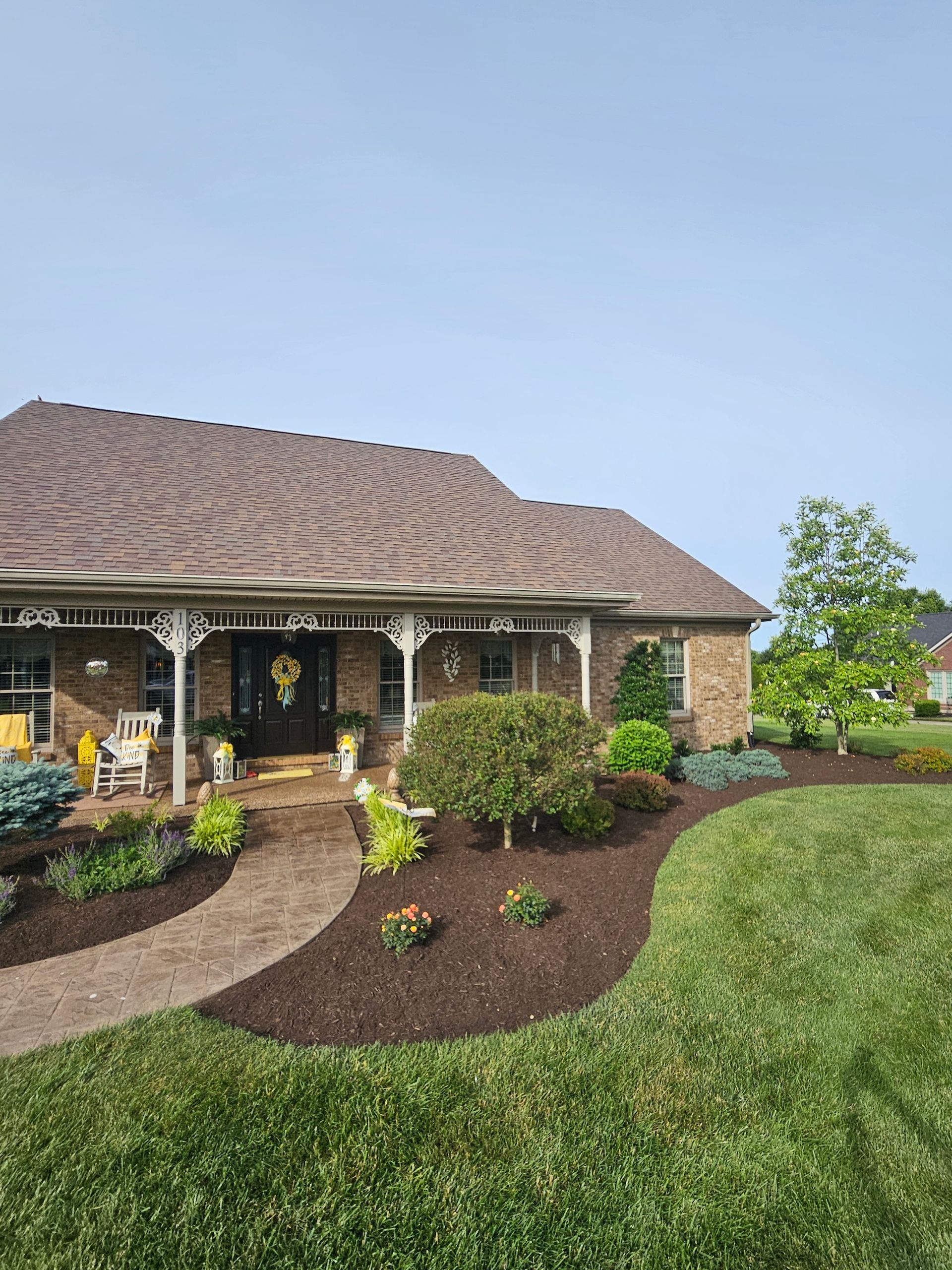 Landscaped front yard with a brick house, brown roof, and blue sky.