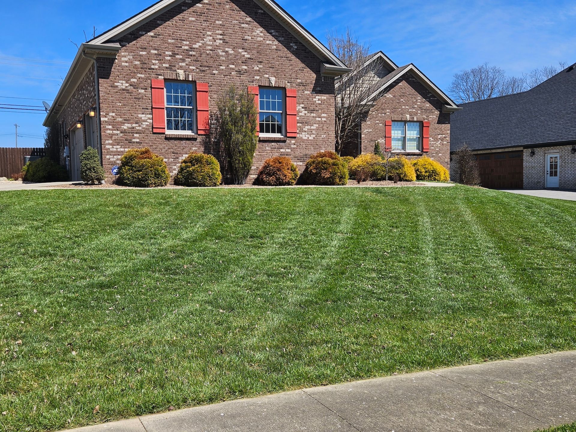 Brick house with well-manicured lawn, red shutters, and a clear blue sky.