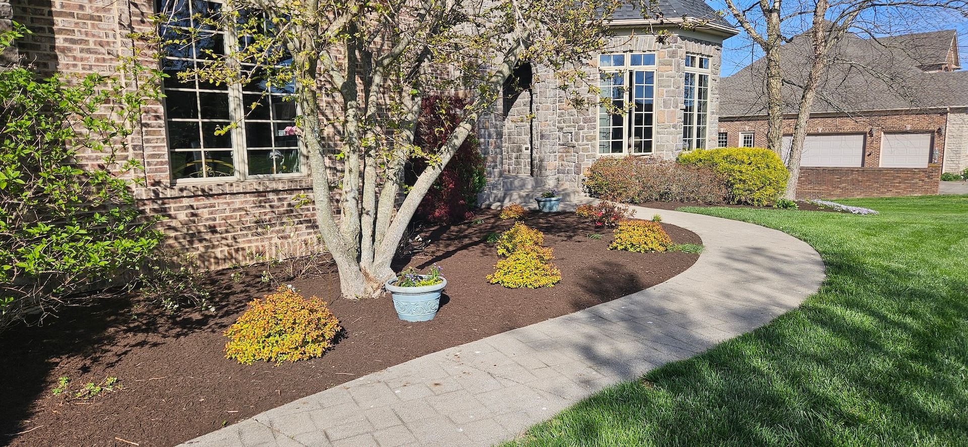A brick house with a curved stone walkway, landscaping, and a grassy lawn.