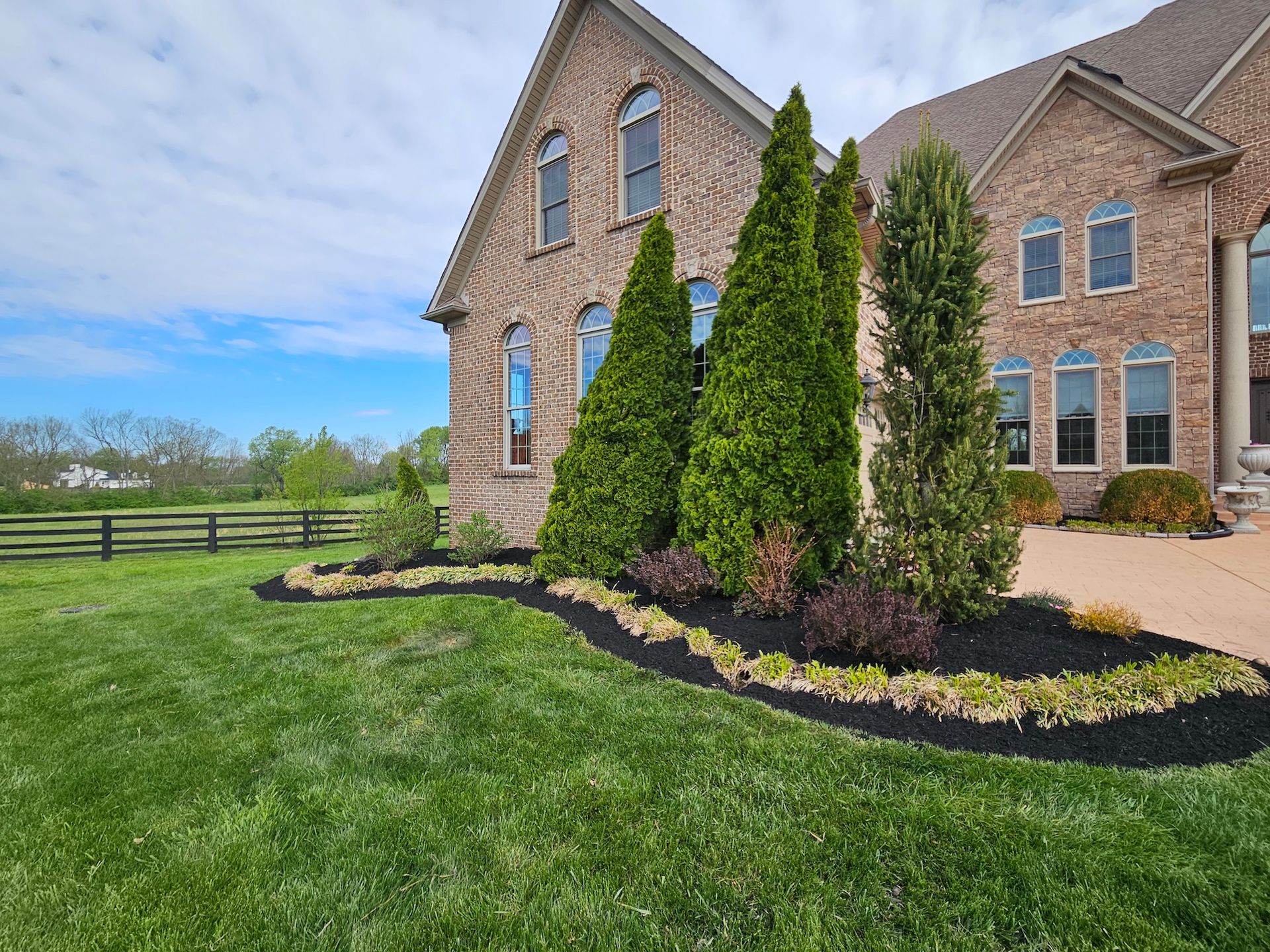 Brick house with landscaped front yard, green lawn, trees, and black mulch.