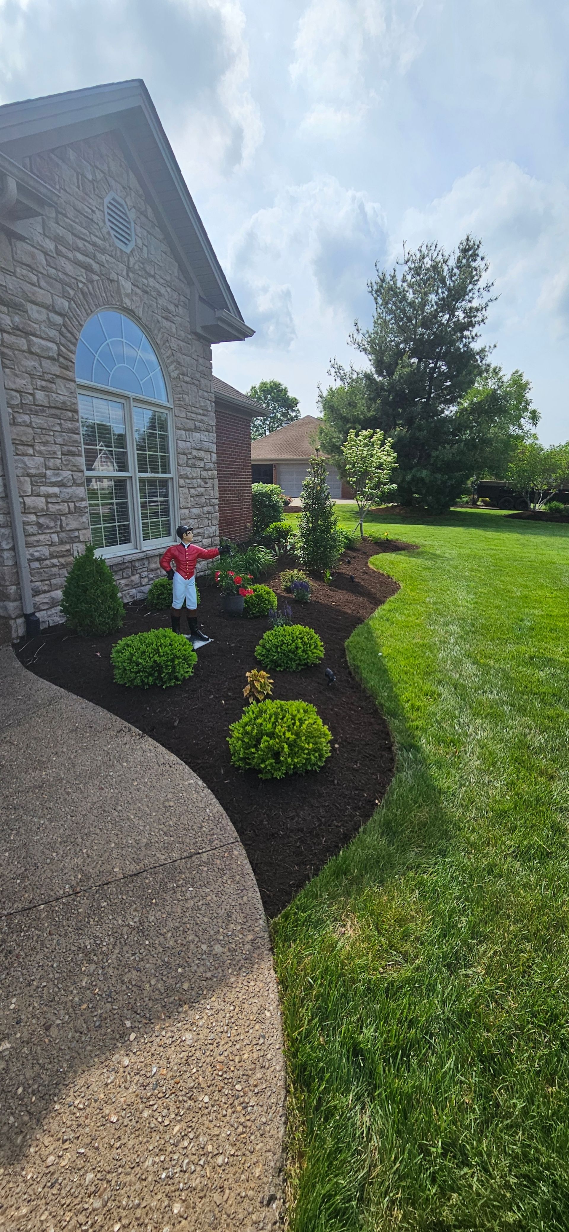 A brick house with a flower bed and green grass in the yard on a sunny day.