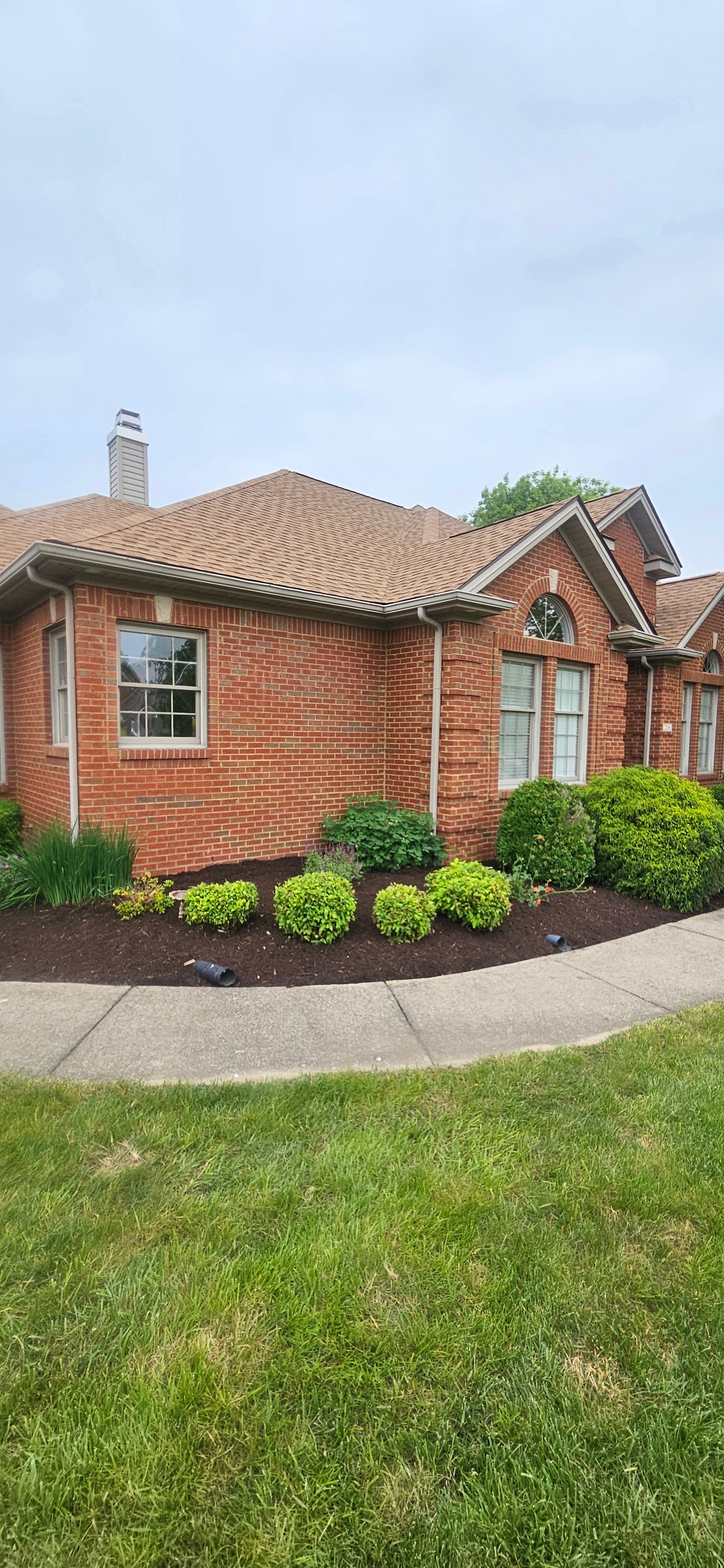 Brick building with patterned brickwork, red-brown roof tiles, and a small yard with green grass and bushes.