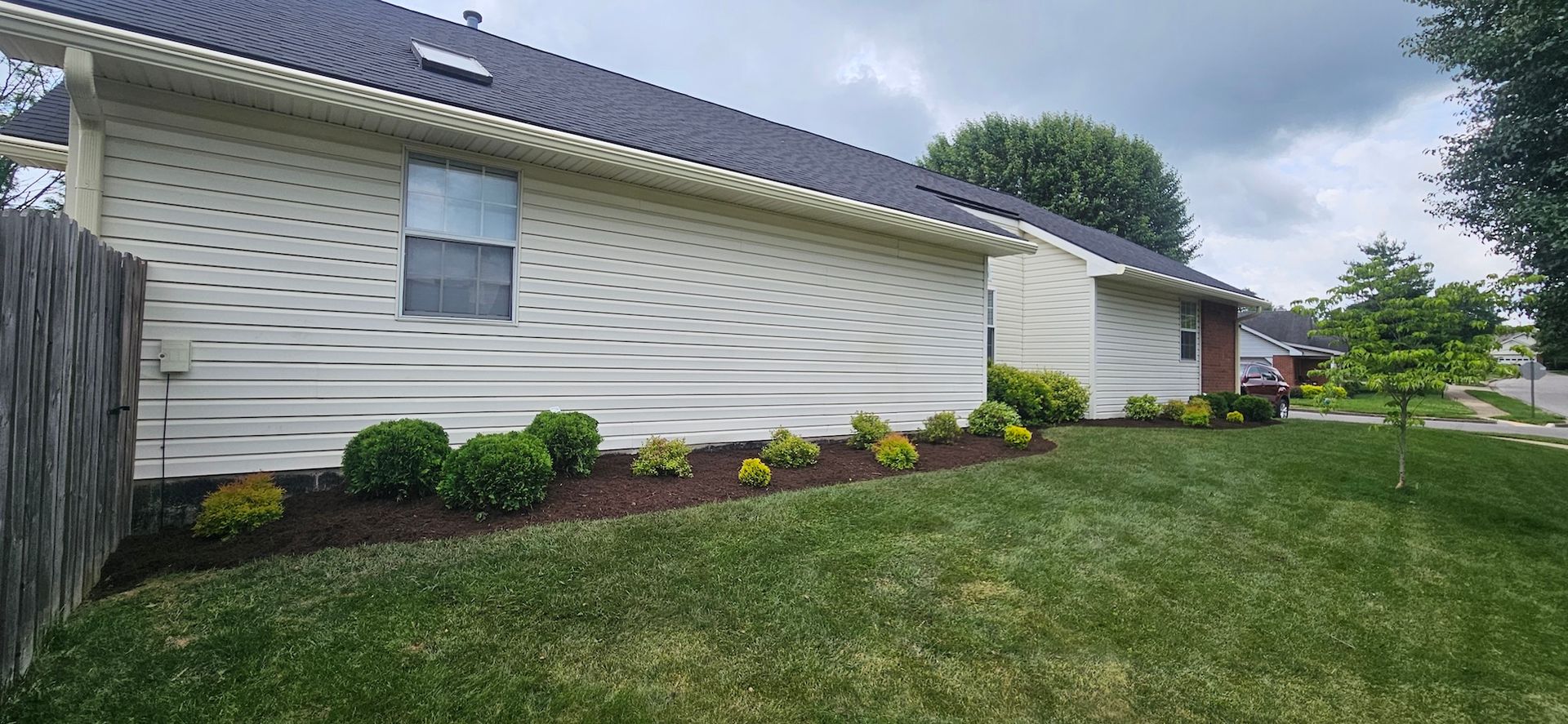A house with cream siding, dark roof, small bushes, and green grass. Overcast sky.
