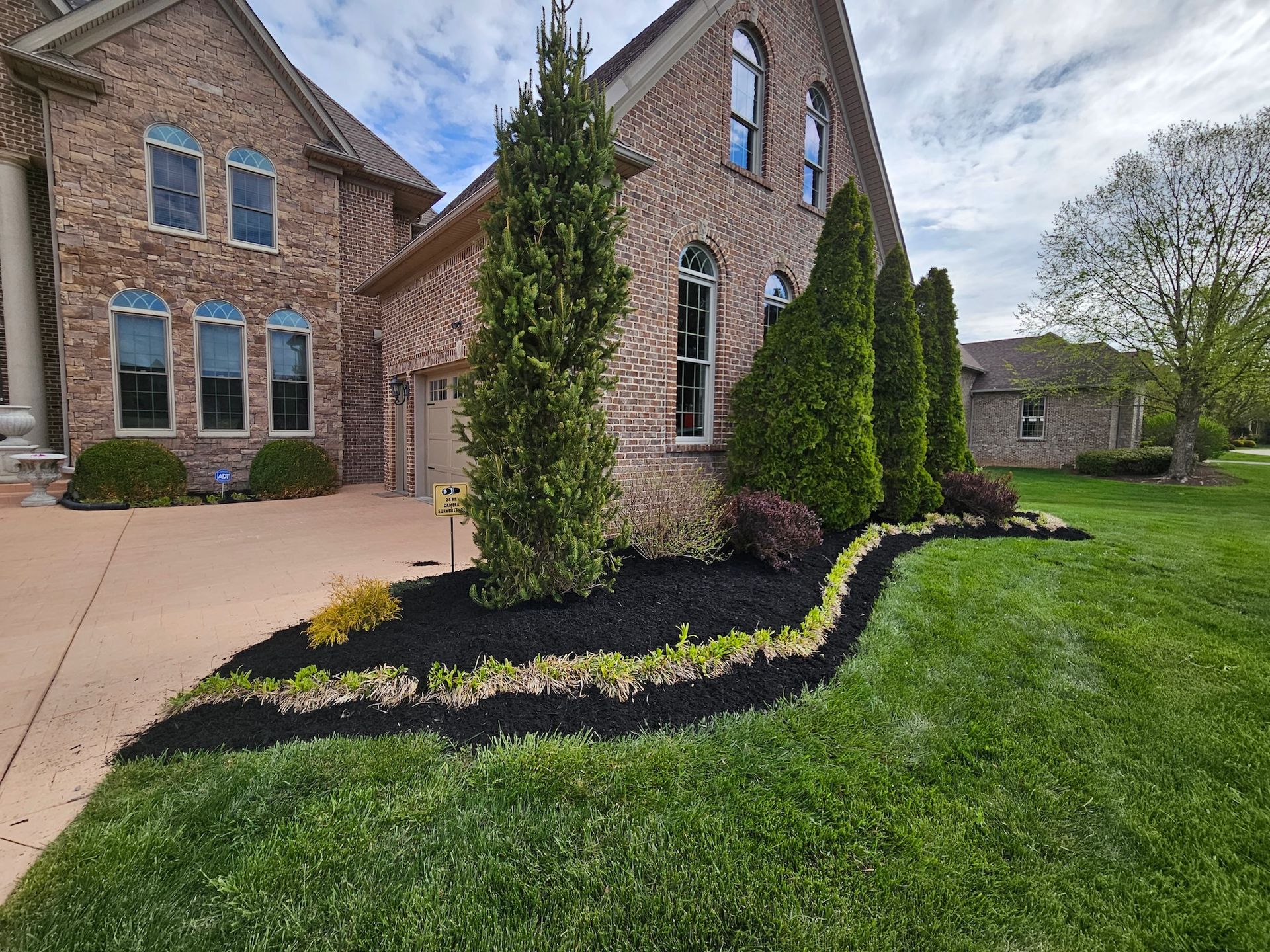 Brick house with manicured landscaping and a green lawn under a cloudy sky.