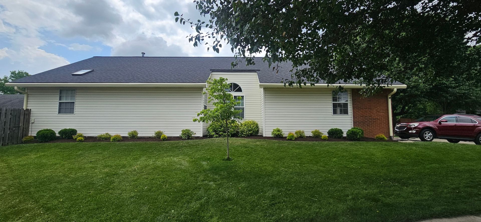 A single-story house with a dark roof and a red car parked nearby.
