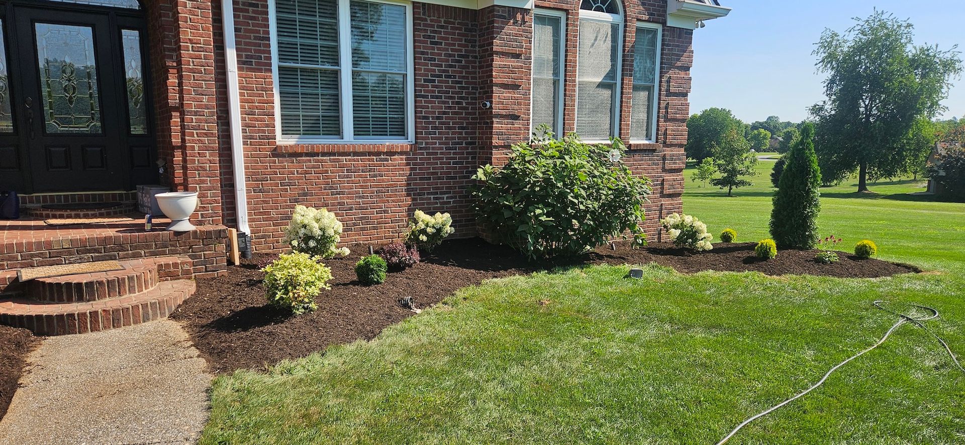 A brick house with a front yard. Landscaping with mulch, bushes, and green grass. Blue sky.