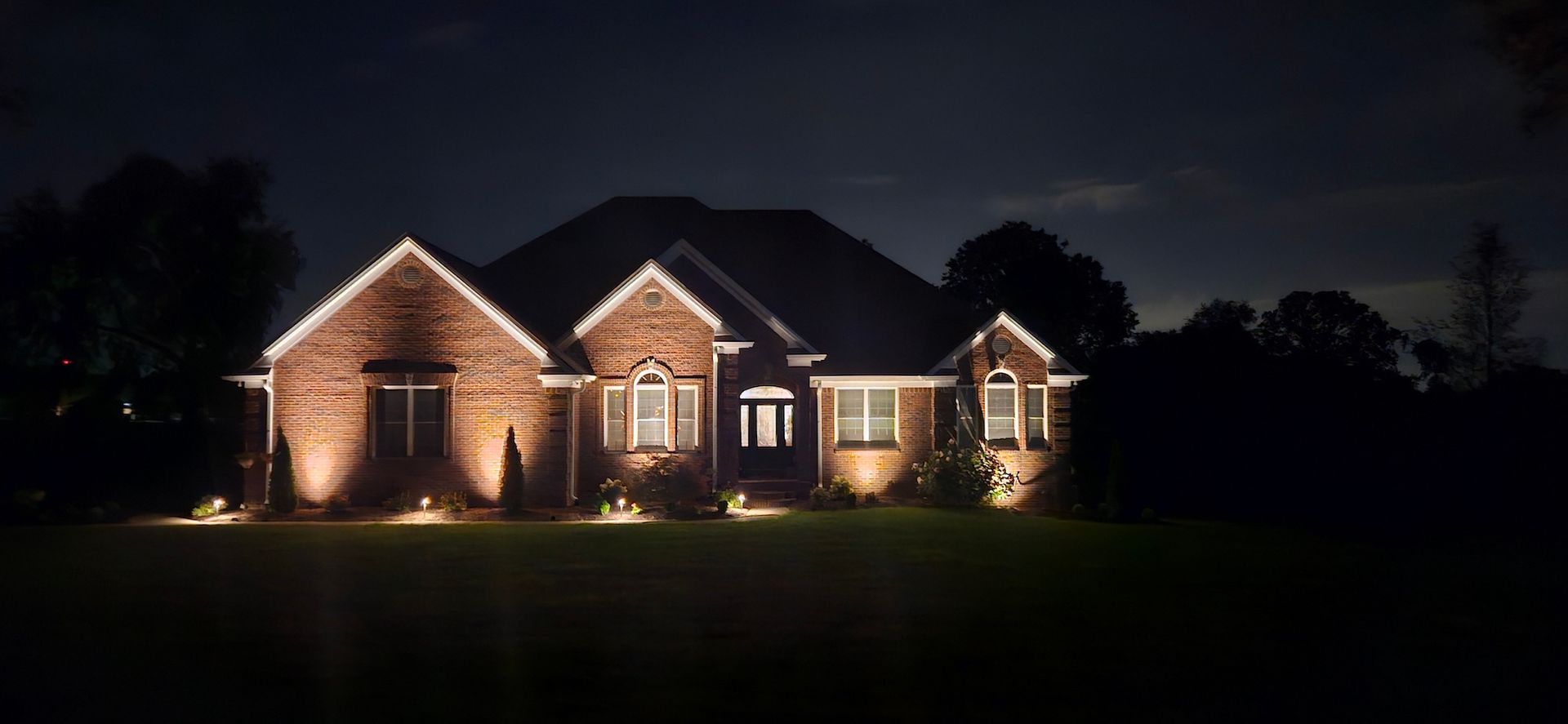 A house is illuminated at night by landscape lighting. Dark sky.